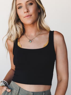 A black cropped tank sits snug against sun-kissed skin, layered with a mustard bralette peeking out at the neckline — the kind of effortless combination that looks accidental but absolutely isn't.