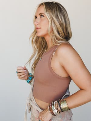 A side-profile shot of a model in a fitted cognac ribbed bralette tank, styled with layered boho bracelets and a delicate pendant necklace — the kind of effortless, jewelry-heavy look that feels totally intentional.