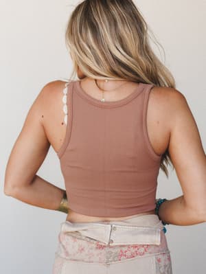 Shot from behind, a ribbed crop tank in warm mauve-cognac pairs with patchwork floral pants — relaxed, sun-warmed, and effortlessly personal.