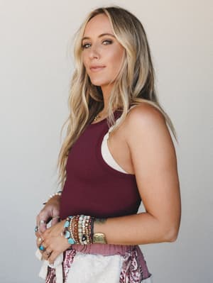 A relaxed, confident close-up of a model in a deep burgundy ribbed tank layered over a white bralette, her wrists stacked with eclectic boho jewelry — the kind of effortless everyday look that feels personal, not put-together.