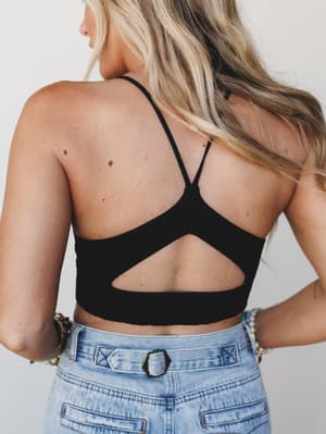 Shot from behind, this black crop bralette steals the show with its open-back cutout and criss-cross spaghetti straps — paired with light wash high-waist denim and stacked boho bracelets for a free-spirited, warm-weather feel.