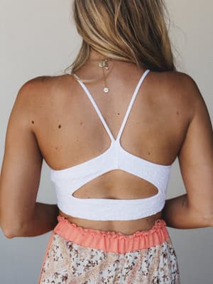 A back-view close-up of a white textured bralette with strappy crossback detail, paired with a coral-waisted floral skirt — effortlessly boho and made for warm-weather days.