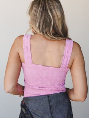 A back-view shot of a textured lavender crop tank with wide straps and a square open back, paired with dark denim — easy, warm-weather dressing with a little personality built into the fabric.
