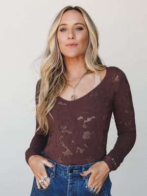 A deep burgundy lace bodysuit layered over a nude cami, paired with high-waist denim and stacked silver and turquoise rings — the kind of effortless mix that looks like it took no effort but definitely did.