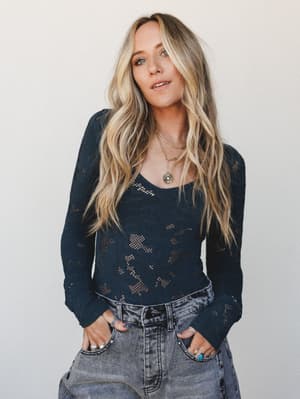 A lived-in, effortlessly cool look — a dark navy open-knit lace bodysuit layered with stacked gold necklaces and worn with washed grey jeans, the kind of outfit that looks intentional without trying too hard.