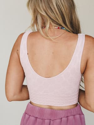 A back-view close-up of a textured crop bralette in soft blush pink, styled with a mauve knit skirt and a colorful beaded necklace — casual and sweet with just enough detail to make it interesting.