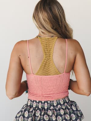 A back-facing shot showing a textured pink crop cami with a bold mustard lace racerback detail, layered over a navy floral skirt — the color mix feels intentional and a little unexpected, in the best way.