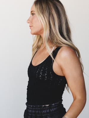 A side-profile shot of a model in a fitted black crochet tank layered over a white bralette, paired with smocked black bottoms — effortless and a little undone in the best way.