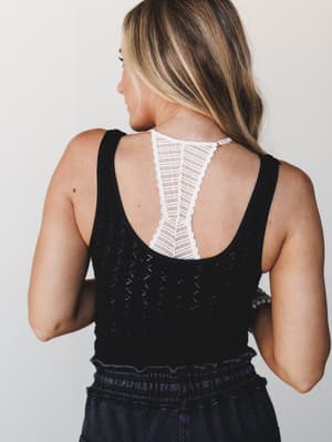 Shot from behind, this look highlights the standout detail: a white crochet lace panel running down the open back of a black knit tank, layered over dark smocked bottoms — effortlessly boho with just enough edge.