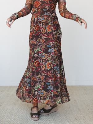A floral mesh maxi skirt in rich chocolate brown sweeps the floor mid-twirl, paired with a matching long-sleeve mesh top and espadrille wedge sandals — the kind of outfit that earns compliments at every door.