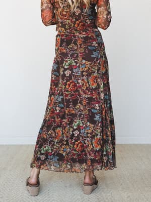 A back-view shot of a flowy chocolate brown floral maxi skirt paired with a matching long-sleeve top and woven wedge sandals — the kind of autumn-ready outfit that feels like it was made for a farmers market and a glass of wine after.
