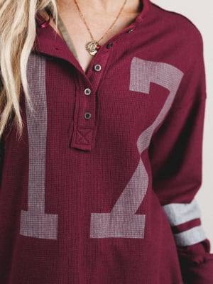 Maroon long-sleeve shirt with large number 12 on a plain background