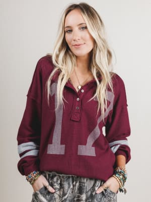 Woman wearing a maroon sweater with a large number 12 on a plain background