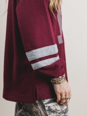 Maroon sweater with white stripes on sleeves, worn by a person with bracelets and rings.