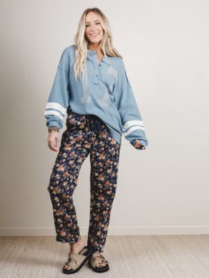 Woman wearing a blue sweater and floral pants standing against a plain background