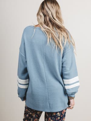 Back view of woman wearing a blue sweater with white stripes on sleeves against a plain background