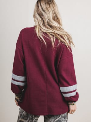 Person wearing a maroon varsity jacket with white stripes on sleeves against a plain background