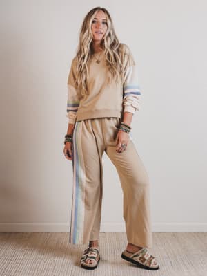 Woman wearing a beige outfit with striped pants against a plain background