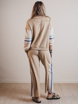 Person wearing a beige tracksuit with blue stripes on a plain background