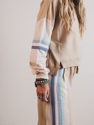 Person wearing a beige jacket with colorful stripes and matching pants on a plain background