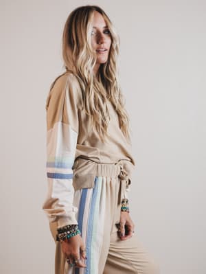 Woman wearing a beige outfit with colorful stripes on a plain background