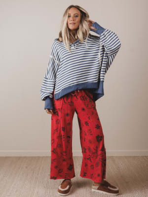 Woman wearing a striped sweater and red floral pants against a plain background
