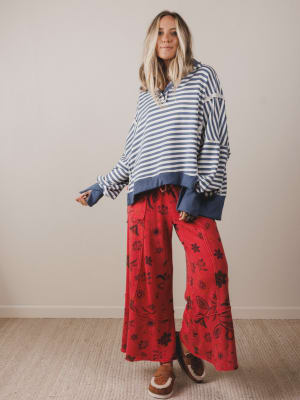 Woman wearing a striped sweater and red floral pants against a plain background