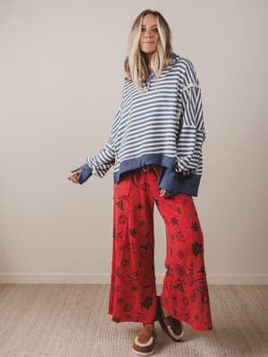Woman wearing a striped sweater and red floral pants against a plain background