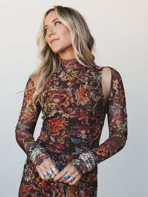 A long-sleeve mesh floral top in deep chocolate brown worn by a blonde model against a neutral studio wall — the kind of piece that looks like it was made for layering over a slip or wearing into a candlelit dinner.