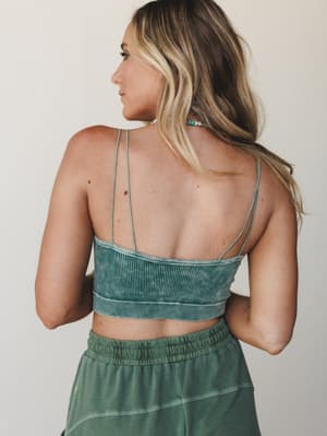 Shot from behind, this mineral-washed ribbed bralette in sage-to-forest green shows off its strappy back detail and easy pairing with a matching skirt — the kind of set that looks effortless whether you're at a summer market or heading into a weekend