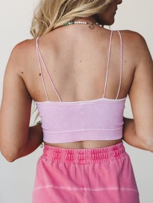 A back-view shot of a ribbed lavender bralette with double spaghetti straps and an open back, paired with pink washed shorts and layered pearl and beaded necklaces — effortlessly warm-weather and personal.