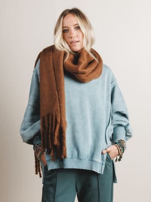 Woman wearing a blue sweater and brown scarf against a plain background