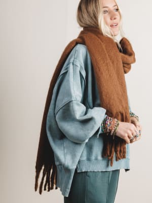 Person wearing a blue sweater and brown scarf with a neutral background