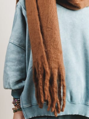 Person wearing a light blue sweater and brown scarf with a neutral background