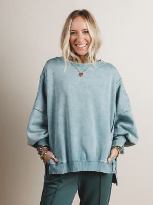 Woman wearing a light blue sweater and green pants against a beige background