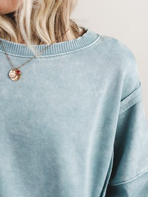 Light blue sweatshirt worn by a person with a necklace featuring a circular pendant.