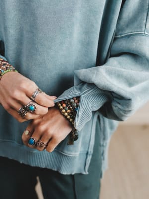 Close-up of hands wearing multiple rings and bracelets with a light blue sweater.