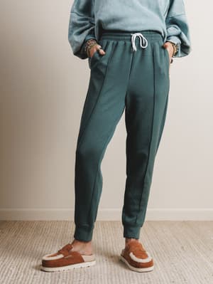 Person wearing teal jogger pants and brown shoes on a neutral background