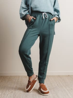 Person wearing teal sweatpants and brown shoes on a neutral background