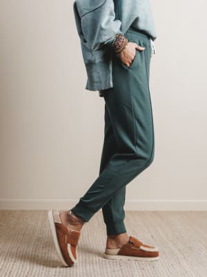 Person wearing teal jogger pants and brown shoes on a neutral background
