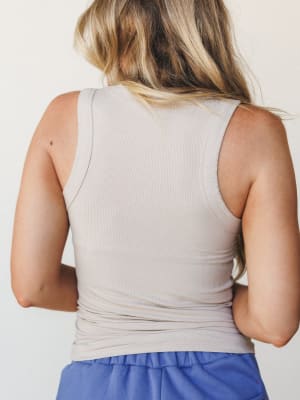 A back-view shot of a fitted ribbed tank in soft taupe, paired with a glimpse of periwinkle blue bottoms — simple, clean, and the kind of top that quietly holds an outfit together.