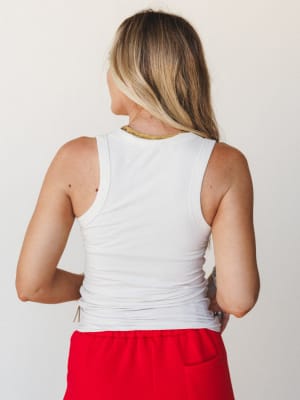 A back-view shot of a model in a fitted white ribbed tank tucked into red wide-leg pants, shot against a clean white wall — simple, confident, and effortlessly put-together.