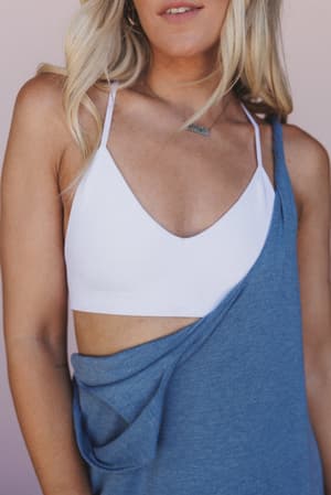 A woman with long blonde hair wears the Crescent Moon Tattoo Bralette in white, paired with a blue off-the-shoulder top. The image is cropped from shoulders to waist, showing her face partially.