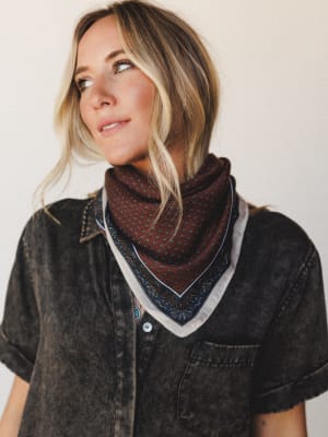 A layered bandana scarf styled at the neck over a washed black denim shirt — the kind of effortless accessory moment that looks intentional without trying too hard.