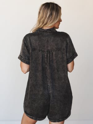 A back view of a relaxed acid wash two-piece set in deep ash black — the oversized short-sleeve button-down top has a gathered yoke detail and cuffed sleeves, paired with matching shorts, giving off that effortless off-duty energy.