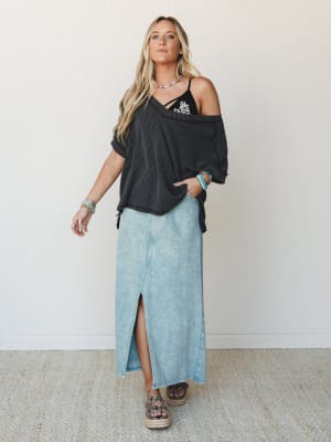 A relaxed full-body outfit layered with a charcoal ribbed off-shoulder top over a black embroidered cami, paired with a washed denim maxi skirt and platform espadrilles — styled with turquoise and beaded accessories for that effortlessly collected bo