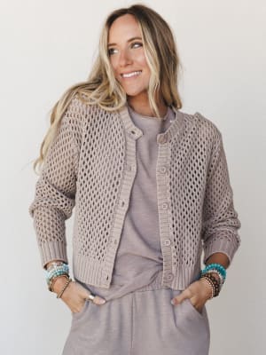 A relaxed, effortlessly layered look — an open-knit cropped cardigan worn over a soft matching tee and wide-leg pants in a warm taupe, styled with stacks of colorful beaded bracelets for a personal, lived-in feel.