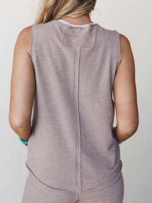 Back view of a soft mauve-gray sleeveless tank with exposed seam detailing and a back patch tab, styled as part of a matching set with turquoise beaded bracelets adding a subtle boho touch.
