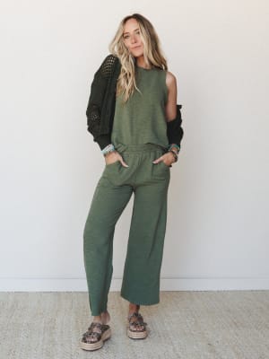 A relaxed olive matching set — sleeveless tank and wide-leg pants — layered with a black open-knit cardigan draped off one shoulder, styled with platform espadrille slides and a stack of beaded bracelets for an effortlessly put-together everyday look