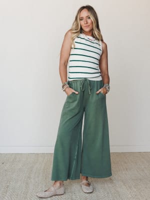 A relaxed full-body shot of a model in a cream stripe sweater tank and wide-leg olive green drawstring pants, styled with woven flats and layered beaded jewelry — effortless and put-together at the same time.